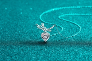 Macro detail of silver S925 heart pendant with moissanite bow on teal glitter surface