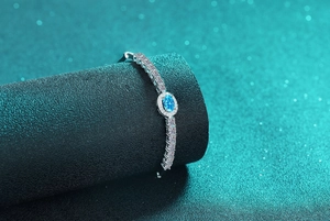 Detailed close-up of a blue oval moissanite silver halo tennis bracelet on a black stand