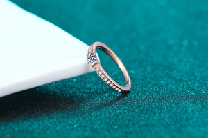 Detail of rose gold moissanite ring with four-prong setting and pavé side stones