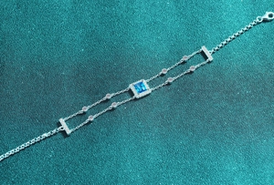 Macro detail of S925 sterling silver bracelet featuring a square blue moissanite and double chain