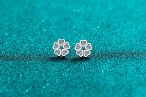 Macro shot of silver heart petal stud earrings with zircon stones on green background