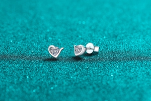 Close-up of heart-shaped S925 sterling silver moissanite stud earrings on teal background