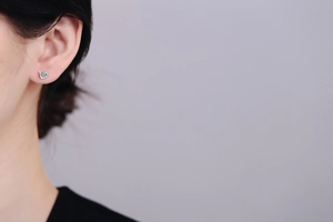 Close-up of heart-shaped silver stud earring with sparkling round zircon on model's ear