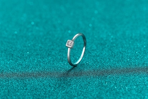 Close-up of square cut moissanite ring with minimalist silver band on teal background