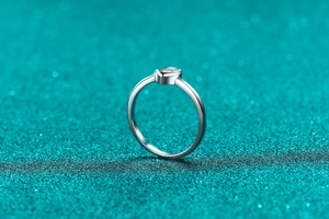 Macro shot of minimalist silver heart ring with a round moissanite in bezel setting
