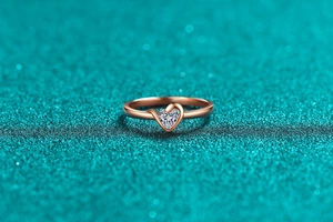 Makroaufnahme eines herzförmigen Moissanit-Rings in Roségold auf blauem Glitzergrund