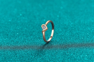 Makroaufnahme von roségoldenem Herzring mit brillantem runden Diamanten auf Glitzergrund