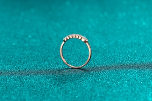 Close-up of rose gold moissanite eternity ring with round cut stones on a teal background