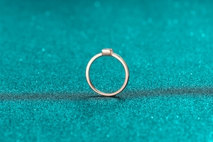 Detail shot of a minimalist rose gold Moissanite ring on a textured teal background