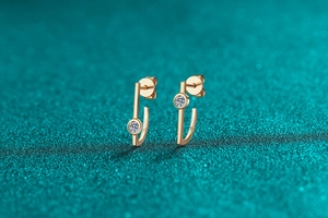 Macro shot of minimalist irregular champagne gold earrings with moissanite on green glitter
