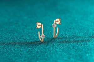 Macro view of J-shaped gold-plated stud earrings with round moissanite inlays