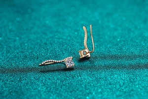 Détail de boucles d'oreilles courbées en or rose avec pavé de pierres et moissanite