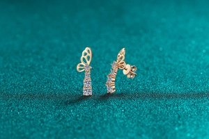 Detail of rose gold butterfly earrings with three dangling round cut zircons on teal base