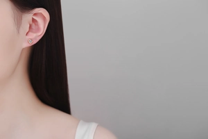 Close-up of heart-shaped gold stud earring with round moissanite on female ear