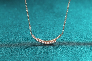 Macro detail of rose gold smile necklace with pave-set crystals on blue background