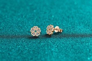 Close-up of rose gold five-petal flower earrings with zircon hearts on blue background