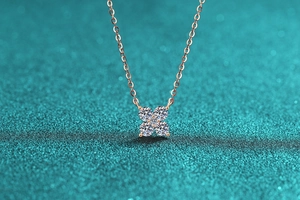 Detail of rose gold clover necklace with four sparkling stones on blue background
