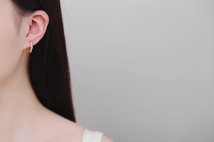 Detail of a gold hexagonal hoop earring with white diamonds on a model's ear