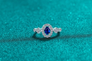 Macro shot of oval blue stone ring with diamond halo and floral side accents