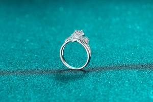 Macro shot of silver pear-cut moissanite ring with a V-shaped crown setting on blue fabric