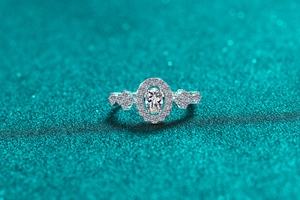 Macro shot of oval moissanite ring with halo setting on shimmering teal background