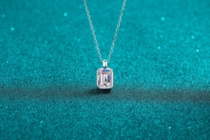 Close-up of emerald cut moissanite pendant with four-prong setting on silver chain