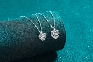 Macro view of two heart-shaped moissanite pendants on O-chains over a teal surface
