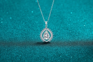 Macro shot of a pear-shaped moissanite necklace with a diamond halo on a teal background