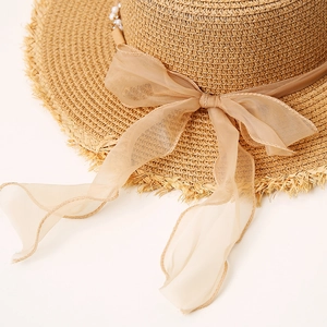 Detail of straw hat with oversized tulle bow, pearl charms and raw fringe edges