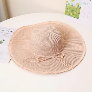 Detail of wide brim straw sun hat with frayed edges and beige bow accent for beach