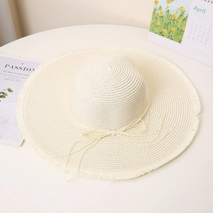 Detailed texture of beige wide brim straw hat with fringe edge and delicate bow tie