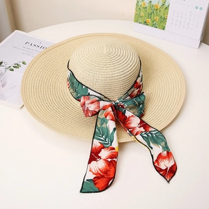 Detail of beige straw sun hat featuring elegant red tropical floral ribbon and large bow
