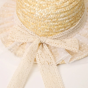 Close-up of flat straw boater hat with cream lace bow and white polka dot mesh trim