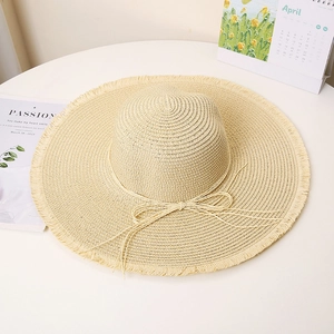 Detail of beige straw hat featuring frayed edges, a delicate bow, and wide sun brim