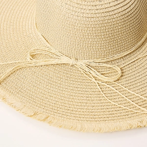 Close-up of beige straw sun hat featuring fringe edges and a delicate bow detail
