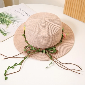 Vue détaillée du chapeau de paille rose avec vigne de feuilles vertes et nœud floral