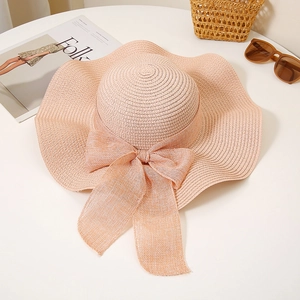 Detail of honey pink wide brim straw hat with elegant wavy edge and bow on white desk