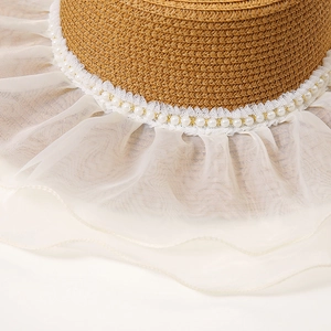 Detail of straw hat featuring elegant white lace, pearl trim and layered mesh brim