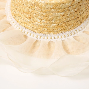 Détail d'un chapeau de paille plat avec garniture de perles et bord en maille d'organza