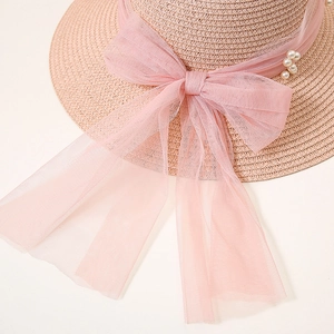 Detail of pink straw sun hat featuring a large mesh bow and decorative white pearls