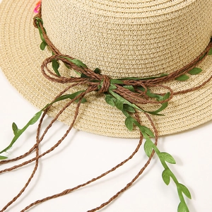 Détail d'un chapeau de paille avec cordon de vigne marron, feuilles vertes et un nœud