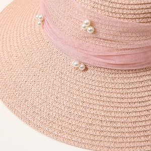 Close-up of pink straw hat with mesh band and pearl details for a summer elegant look
