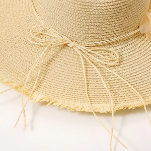 Close-up of beige straw sun hat featuring woven lace flowers and frayed edge detail