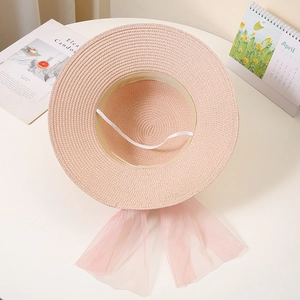 Detail of pink straw sun hat featuring wide brim, elastic chin strap and large mesh bow