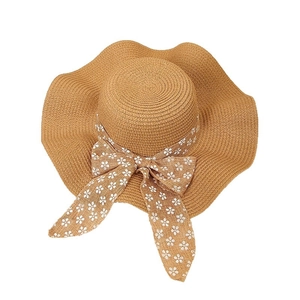 Women's summer straw sun hat with wide wavy brim and floral bow ribbon on white background