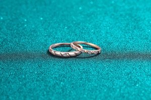 Close-up of rose gold couple rings with textured bands and diamond accents on blue background