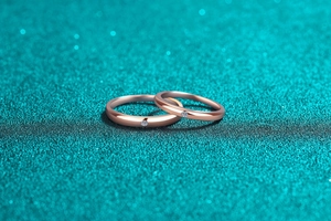 Close-up of champagne gold couple rings with small diamonds on glittery green background