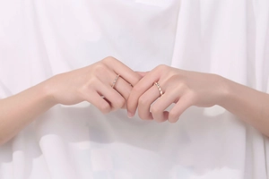 Close-up of 18K gold moissanite rings on hands with elegant folded fabric backdrop
