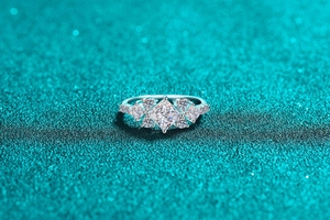 Macro shot of silver princess cut moissanite ring with side stones on teal glitter