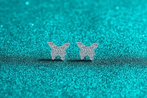 Macro shot of silver butterfly stud earrings with sparkling moissanite on green glitter
